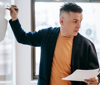 A trainer at a whiteboard, notes in hand, mid-explanation to a group