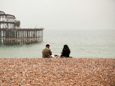 Two people sitting on Brighton's pebble beach, looking out to sea towards the West Pier
